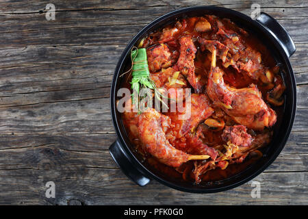 Italian Style Braised Rabbit With leek, chopped tomatoes, herbs and mushrooms in dutch oven on old dark wooden table, view from above Stock Photo