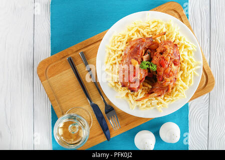 delicious Rabbit legs braised with vegetables and herbs, served with pasta on white plate on chopping board with glass of white wine, healthy recipe,  Stock Photo