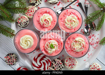 close-up of Christmas no bake strawberry Cheesecake Mousse topped with whipped cream, sprinkled with crushed candy canes in glass cups on tray with sp Stock Photo