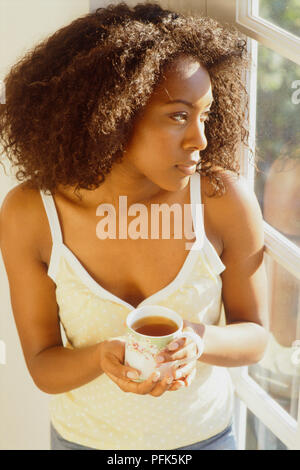 Woman holding cup of tea looking out of window Stock Photo