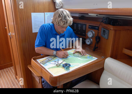 Blonde man in blue shirt sitting with map, using measuring instruments Stock Photo