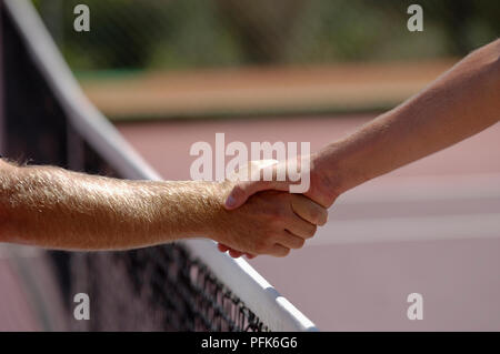 Tennis players shaking hands over net, close-up, Stock Photo