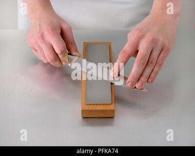 Hands sharpening knife on sharpening block, close-up Stock Photo