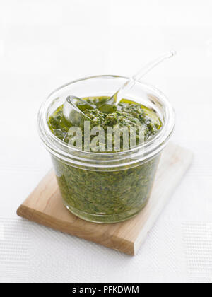 Salsa verde in glass jar, with spoon, on wooden board, close-up Stock Photo