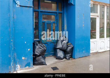 Full bin bags rubbish bags, dumped rubbish piled in a doorway in Skibbereen, West Cork, Ireland with copy space; Stock Photo