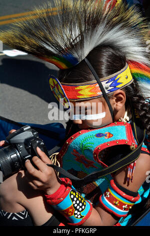 A young Native-American boy wearing traditionall Plains Indian regalia takes a picture with his Nikon camera. Stock Photo