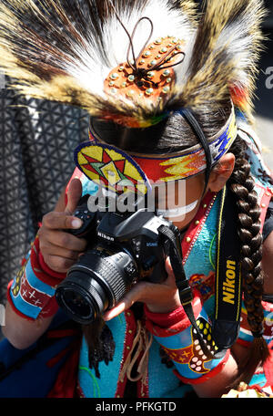 A young Native-American boy wearing traditionall Plains Indian regalia takes a picture with his Nikon camera. Stock Photo