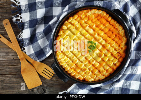 delicious shepherd's pie or cottage meat pie in baking dish on dark wooden table with kitchen towel and wooden spatulas , authentic recipe of english  Stock Photo