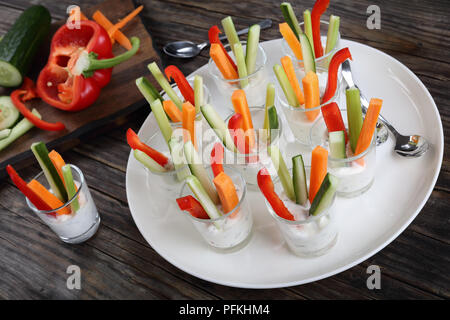 individual Cocktail shot glasses with tartar spicy sauce and colorful vegetables sticks on platter with ingredients on cutting board, view from above Stock Photo
