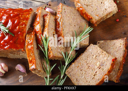 sliced meatloaf on dark wooden cutting board  with garlic, rosemary, and tomato sauce, traditional holiday recipe, view from above Stock Photo