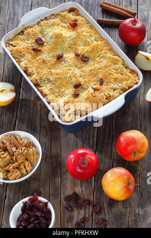 delicious apple crumble or apple crisp in baking dish with ingredients on dark wooden table, vertical view from above Stock Photo