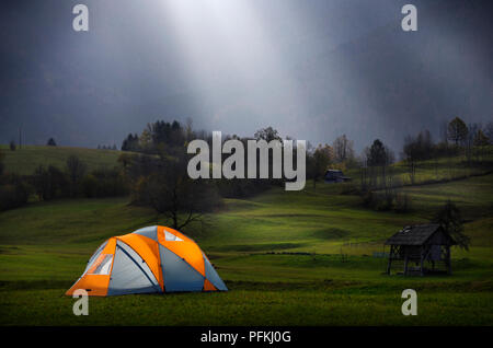 Rays of sunlight beaming down from overcast sky onto dome tent pitched in field Stock Photo