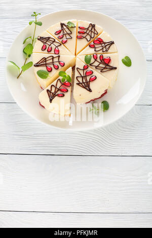 delicious ornately decorated cheesecake with fresh green mint leaves on white platter on wooden table, vertical view from above Stock Photo