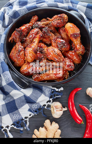 savory grilled crispy chicken drumsticks sprinkled with sesame seeds in black brazier on wooden table with ingredients for teriyaki sauce, view from a Stock Photo