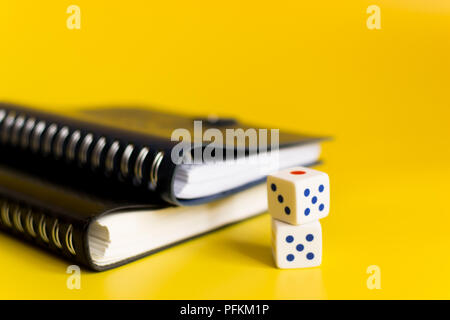 black and blue notebooks on a yellow background with white dice to calculate the bet Stock Photo