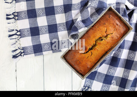 freshly baked delicious banana bread with walnuts and chocolate pieces in a loaf pan with kitchen towel on wooden worktop, authentic recipe, view from Stock Photo