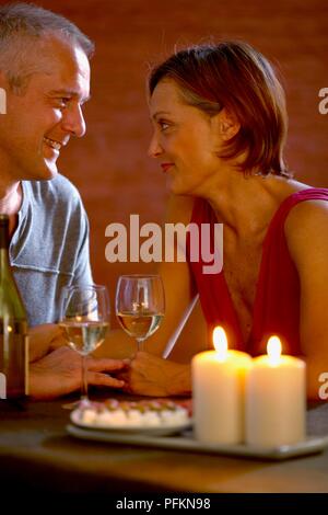 Woman and man sitting at table holding wine glasses looking in each other's eyes Stock Photo