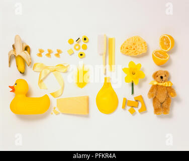 Selection of yellow objects, bath sponge, Daffodil, uninflated balloon, rubber duck, semi-peeled banana, sweets, uncooked pasta, ribbon, teddy bear, halved Lemon, comb. Stock Photo