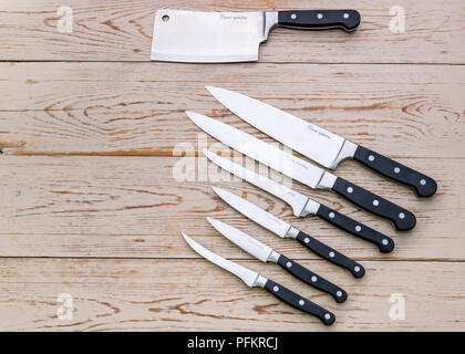 An assortment of various kitchen knives on a wooden background.