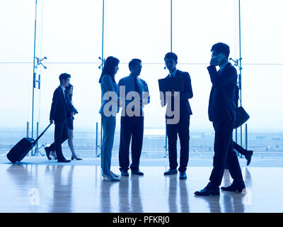 silhouettes of asian corporate executives discussing business in airport terminal building. Stock Photo