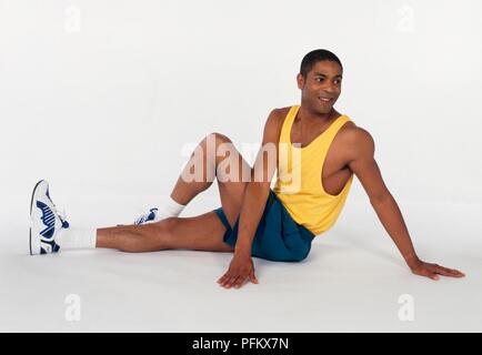 Young man sitting on the ground performing trunk-twist stretch exercise Stock Photo