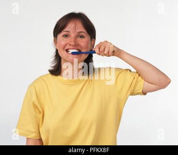 Woman in t-shirt cleaning her teeth, front view, looking at camera Stock Photo