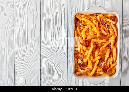 aussie fries smothered in melted cheese and bacon in a baking dish on a white wooden table, view from above, flat lay Stock Photo