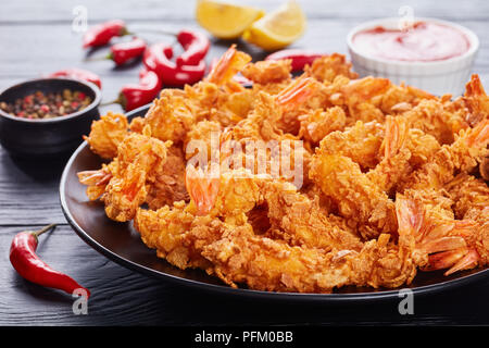 delicious crunchy corn flakes breaded and deep-fried shrimps on a black plate on a black wooden table with ketchup in bowl and chili peppers at the ba Stock Photo