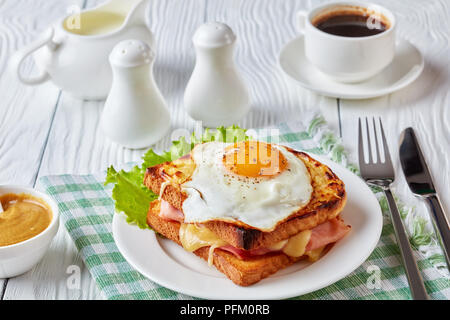 delicious breakfast - hot french toasts croque madame with ham, melted emmental cheese and fried sunny side up egg served on a white plate with cup of Stock Photo