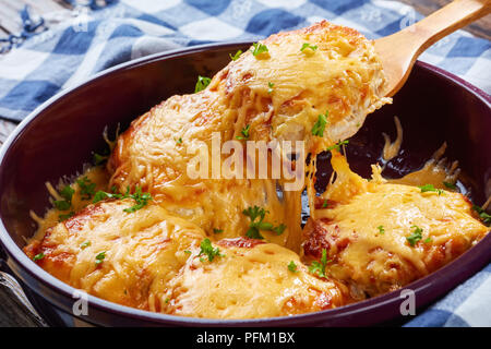 Pork Chop Topped with Onions, Mayo and melted Cheese on a wooden spoon in a baking dish on a old dark wooden table, view from above, close-up Stock Photo