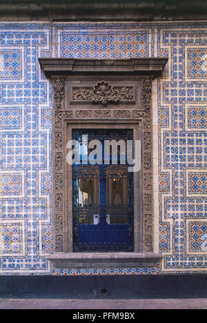 Mexico, Mexico City, Casa de los Azulejos or House of Tiles, 16th century window with ornate metal screen and carved stone frame on a wall of patterned blue tiles. Stock Photo