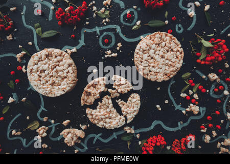 Flat lay crunchy rice cakes on dark wooden background with floral arrangement background, overhead top down view Stock Photo