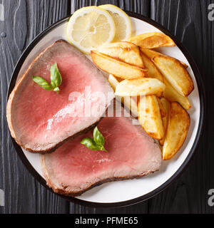 Medium roasted beef steak with potatoes close-up on a plate on a black table. top view from above Stock Photo