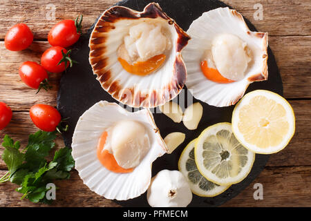 Sea delicacies raw scallops in a seashell and fresh vegetables on a table. Horizontal top view from above Stock Photo