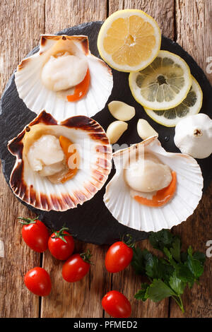 Sea delicacies raw scallops in a seashell and fresh vegetables on a table. vertical top view from above Stock Photo