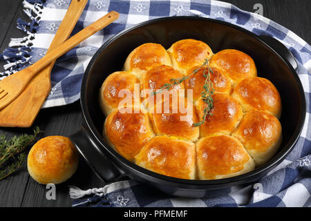 delicious freshly baked golden brown soft and fluffy homemade dinner rolls in baking dish with kitchen towel and spatulas on wooden kitchen table, vie Stock Photo