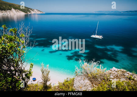 Fteri beach, Cephalonia Kefalonia, Greece. White catamaran yacht in clear blue sea water. Tourists on sandy beach near azure lagoon Stock Photo