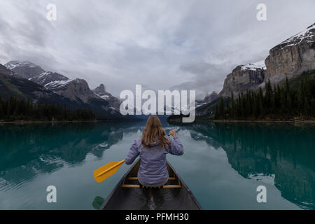 A white female holding a canoe paddle on Maligne Lake in Jasper National Park surrounded by mountains Stock Photo