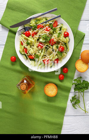 delicious fresh macaroni salad with cucumber slices, celery sticks, tomato and bean sprouts on white plate with toasted buns and sesame oil on wooden  Stock Photo