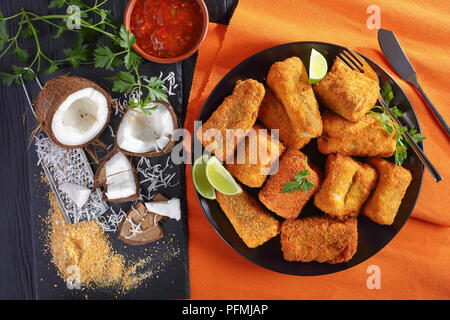 close-up of delicious pieces of crispy fried fish coated with coconut bread crumbs.  ingredients and homemade mango sauce at background, view from abo Stock Photo