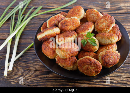 delicious roasted hot meat cutlets on black plate, on old wooden table with spring onion, view from above, close-up Stock Photo