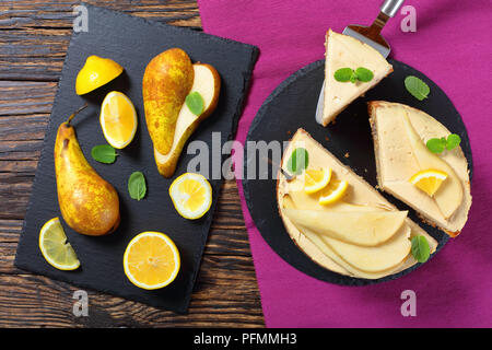 homemade pear sponge cake with cream cheese, decorated with mint, pear and lemon slices cut in slices on black slate plate, view from above Stock Photo