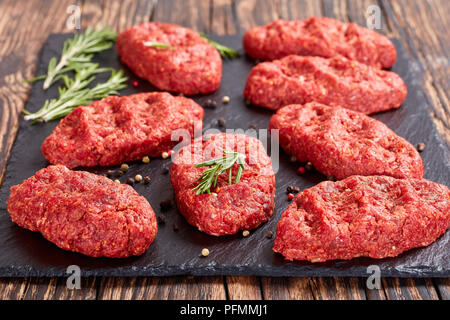 fresh raw salisbury beef steaks on black stone plate with rosemary and peppercorn, side view from above,  close-up Stock Photo