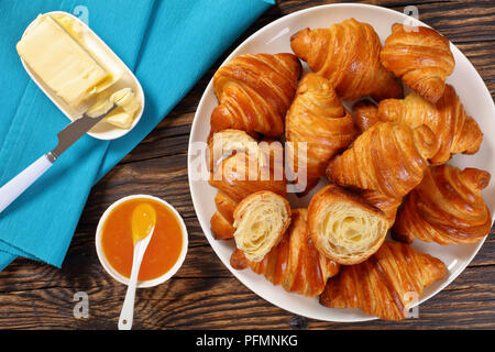 close-up of delicious homemade freshly baked crispy french croissants served  for breakfast on white plate with orange jam and fresh butter on rustic  Stock Photo