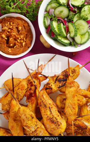 Chicken satay on skewers on a white plate on rustic wooden table served with peanut sauce and cucumber onion salad, authentic recipe, vertical view fr Stock Photo