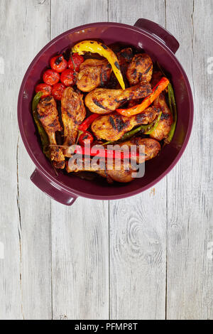 delicious chicken drumsticks roasted in oven in brazier with colorful chili peppers and cherry tomatoes, view from above Stock Photo
