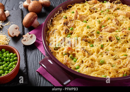 Tetrazzini - pasta, cream sauce, chicken meat, grated cheese, green peas, mushrooms casserole in a baking dish with ingredients at background, classic Stock Photo