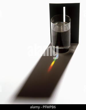 Light beam through glass of water and colour spectrum on black shadow Stock Photo