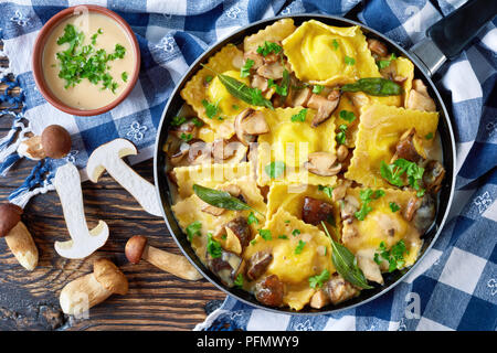 delicious homemade ravioli stuffed with ricotta cheese cooked in creamy garlic mushrooms sauce in a skillet on an old wooden table with kitchen towel  Stock Photo