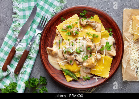 homemade ravioli stuffed with ricotta cheese cooked in creamy garlic mushrooms sauce and served on a plate on a concrete table with napkin and grated  Stock Photo
